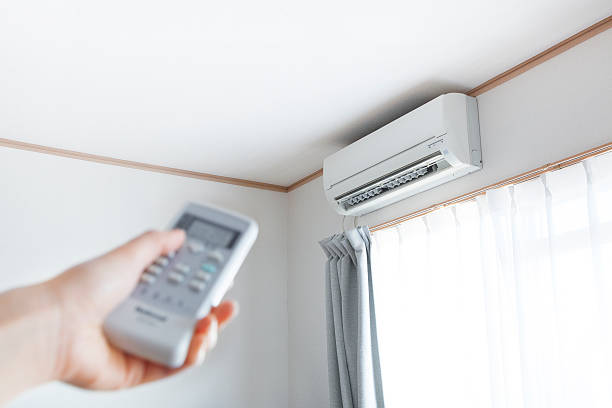 hand pointing a remote control directly at the wall-mounted indoor unit of a mini split air conditioner